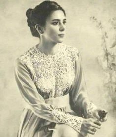 an old black and white photo of a woman in a dress sitting on a chair