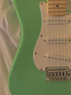 a green electric guitar sitting on top of a white sheet