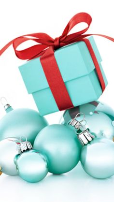 a blue gift box with red ribbon on top of some christmas baubles and ornaments