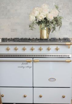 an old fashioned white stove with gold trim and flowers in a brass vase on top