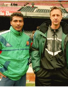 two men standing next to each other in front of an empty stadium bleachers