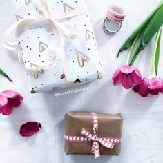 a present wrapped in brown paper and tied with white ribbon next to pink tulips