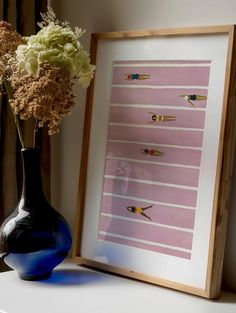 a vase with some flowers in it next to a framed print