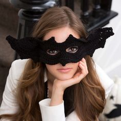 a woman wearing a black crochet bat mask with her hands on her face