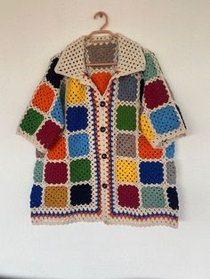 a crocheted jacket hanging on a wall with a coat hanger in front of it