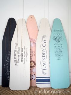 four wooden surfboards are lined up against the wall, one is painted pink, blue and white