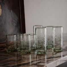 five glasses sitting on top of a marble counter next to a framed painting in the background