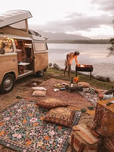 a camper van is parked next to the water with its door open and people around it