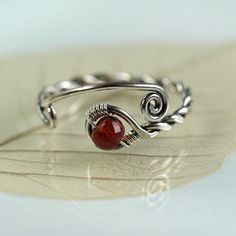 A special silver and garnet ring with a twist and open spiral design. It's adjustable and perfect as a gift if you're not quite sure of the size you need. The shank is twisted from one wire and in the loop at the end is nestled an AA-plus faceted wine red garnet bead and the opposite ends are shaped into spirals. Both twists and spirals are classic and has been used since Celtic times in jewellery. I think my Danish heritage is shining through. :o) Garnet is a stone of positive thoughts which is Red Adjustable Wire Wrapped Rings, Adjustable Red Spiral Jewelry, Adjustable Red Wire Wrapped Rings, Handmade Adjustable Ruby Ring, Handmade Adjustable Silver Ruby Ring, Unique Adjustable Sterling Silver Ruby Ring, Unique Adjustable Ruby Ring In Sterling Silver, Adjustable Open Ruby Ring As Gift, Adjustable Silver Ruby Ring