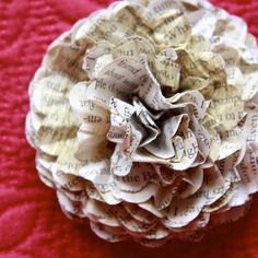 a flower made out of old book pages sitting on top of a red cloth covered table