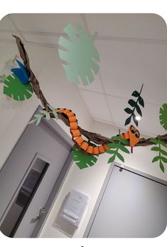 an orange snake on a branch hanging from the ceiling in a room with white walls