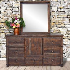 an old dresser with flowers and a mirror on it in front of a stone wall