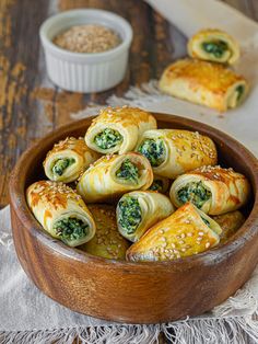 a wooden bowl filled with spinach rolls on top of a table next to bowls of seasoning