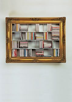 a gold framed book shelf filled with lots of books on top of a white wall