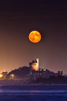 a full moon is seen over a castle on top of a hill in the distance