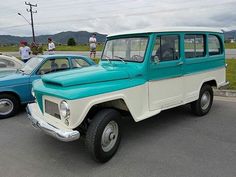 an old blue and white truck parked in a parking lot next to another car on the road