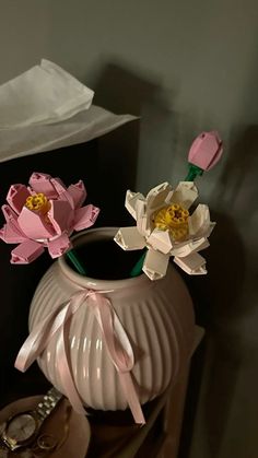 two pink flowers in a white vase on a table next to a box and tissue paper