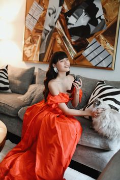 a woman in an orange dress sitting on a couch next to a white and black cat