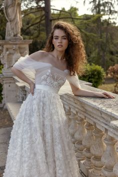 a woman in a white wedding dress leaning on a stone wall with her hands on her hips