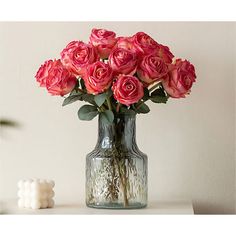 a vase filled with pink roses sitting on top of a table next to a candle