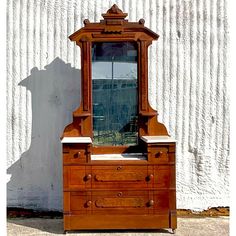 an old wooden dresser sitting in front of a white wall with a mirror on it