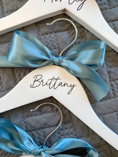 two personalized wooden hangers with blue bows and name written on them, sitting on a quilted surface