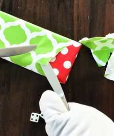 someone is cutting paper with scissors on a wooden table next to a pair of gloves