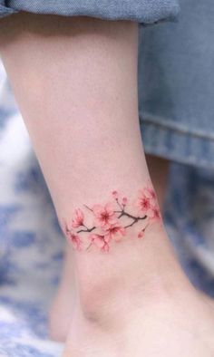 a woman's foot with pink flowers on the side of her leg and an ankle tattoo