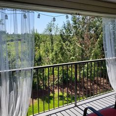 a balcony with chairs and curtains on the outside, looking out at trees in the distance