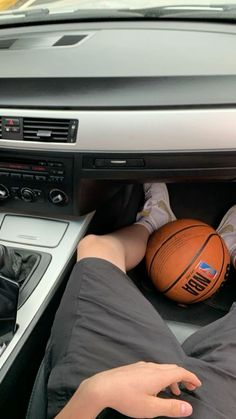 a person is laying down in the car with a basketball on their lap and his feet propped up against the steering wheel