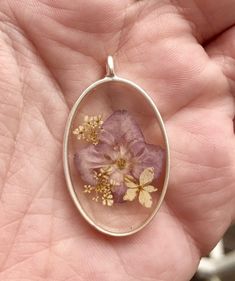 a close up of a person's hand holding a pendant with flowers in it