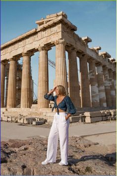 a woman standing on top of a rock next to an ancient building with columns and pillars