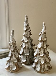 three ceramic christmas trees sitting on top of a white table next to an open window