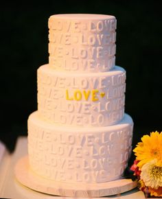 a three tiered white cake sitting on top of a table next to yellow flowers