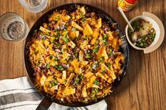 a skillet filled with food on top of a wooden table next to two glasses