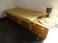 a bed made out of wooden pallets with a lamp on the side and a magazine laying on top