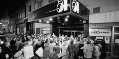 a large group of people standing in front of a building with a sign that says 55 cents