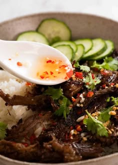 a bowl filled with rice, meat and cucumber garnished with seasoning