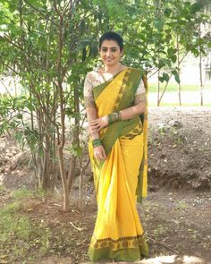 a woman wearing a yellow and green sari standing in front of some tree branches