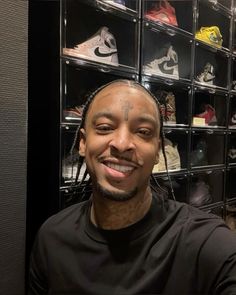 a man with dreadlocks smiles in front of a rack of shoes and sneakers