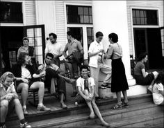 black and white photograph of people sitting on the steps in front of a building with doors