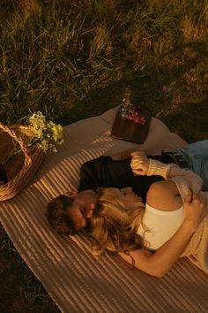 a man and woman laying on a blanket next to each other in the grass with flowers