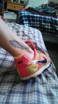 a woman's foot with tattoos on her left leg and nike shoes on the bed