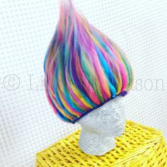 a yellow wicker basket with a colorful hair doll on it's head sitting on top of a white surface