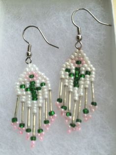 a pair of earrings with green and white beads on them in a box, sitting on top of a table