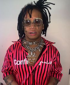 a man with dreadlocks wearing a red and black striped shirt is standing in front of a white wall