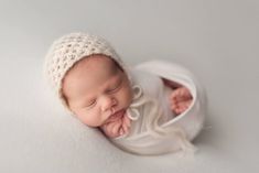 a newborn baby is sleeping in a white bowl and wearing a crochet hat