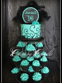 a three tiered cake decorated with blue frosting and black icing, topped with cupcakes