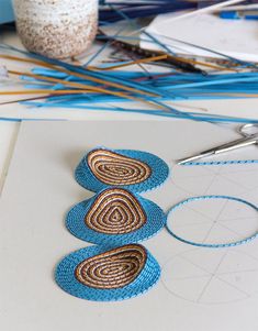 the scissors are next to some blue and brown pieces of yarn on top of paper