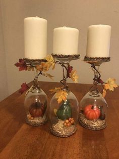 three glass vases filled with candles on top of a wooden table covered in fall leaves